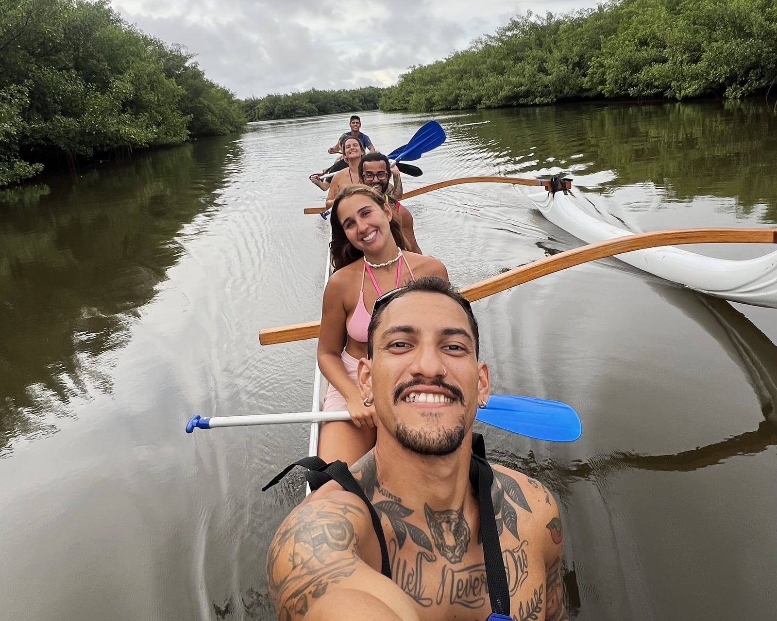 Grupo sorrindo a bordo de uma canoa havaiana em canal de manguezal da Lagoa Guaraíras, em Tibau do Sul (RN)