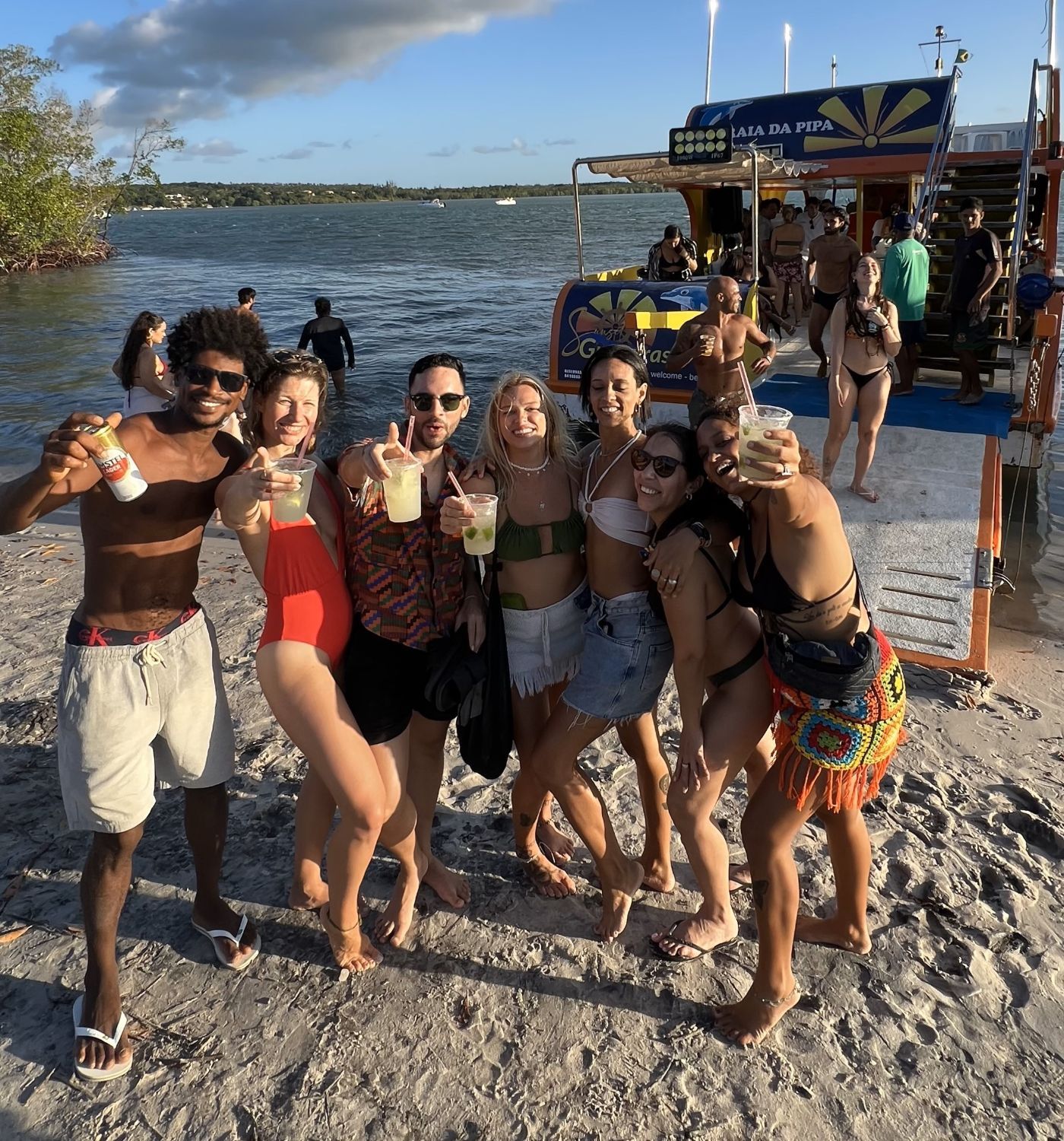 Grupo de amigos brindando na areia ao lado do barco da Festa no Barco, em Pipa
