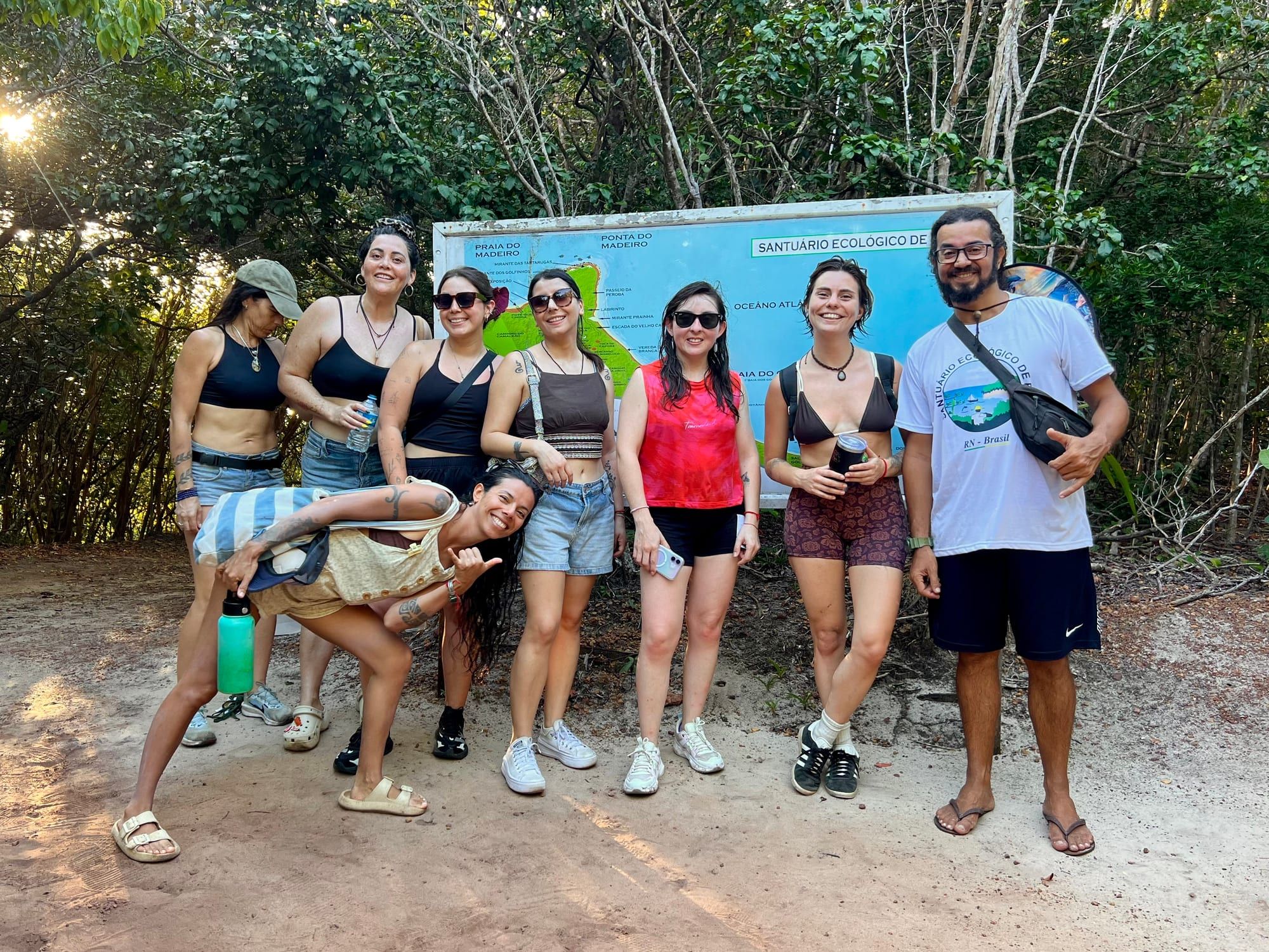 Grupo de viajantes com biólogo local diante da placa do Santuário Ecológico da Pipa
