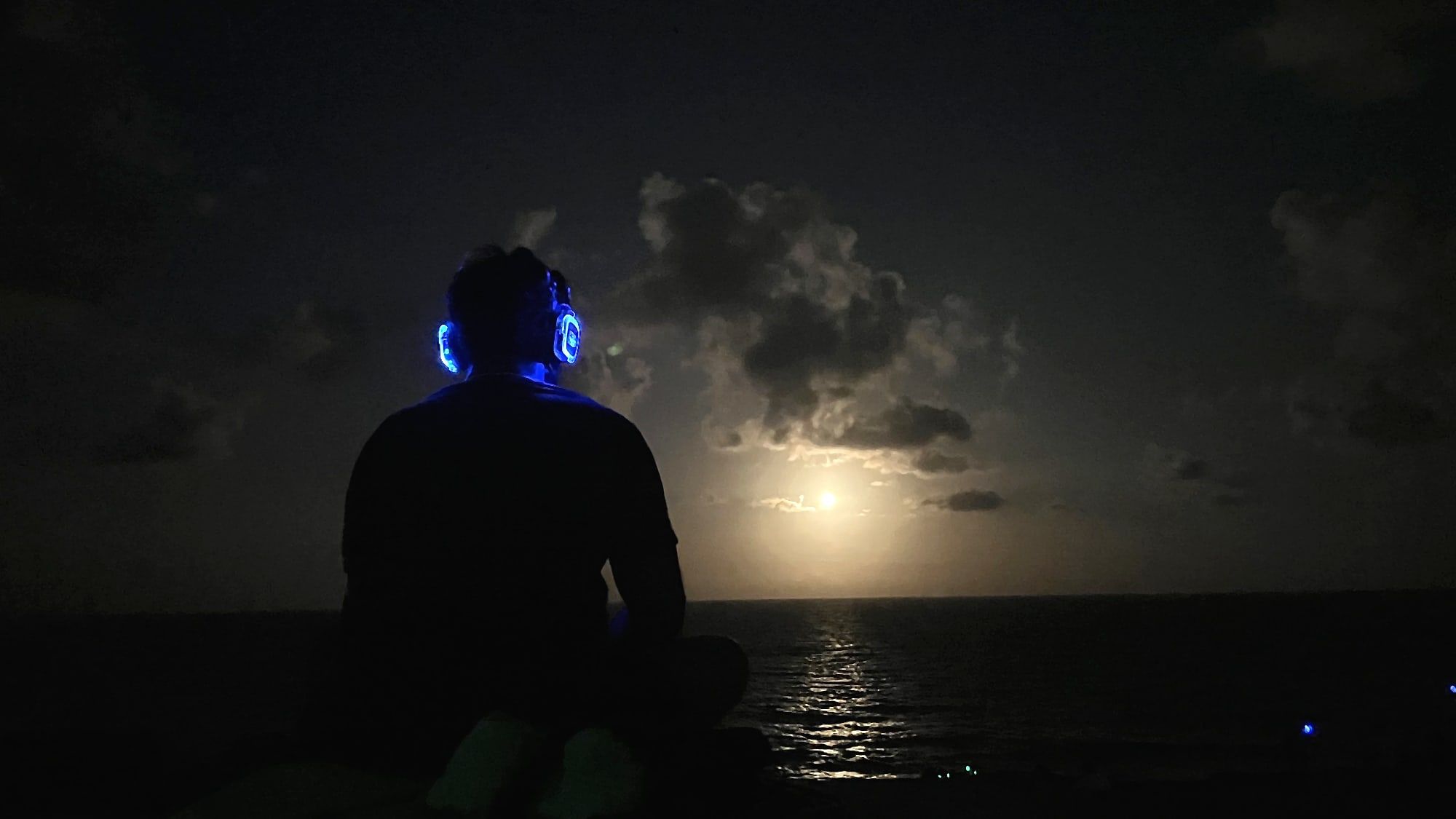 Participante com fone aceso diante da lua cheia sobre o mar