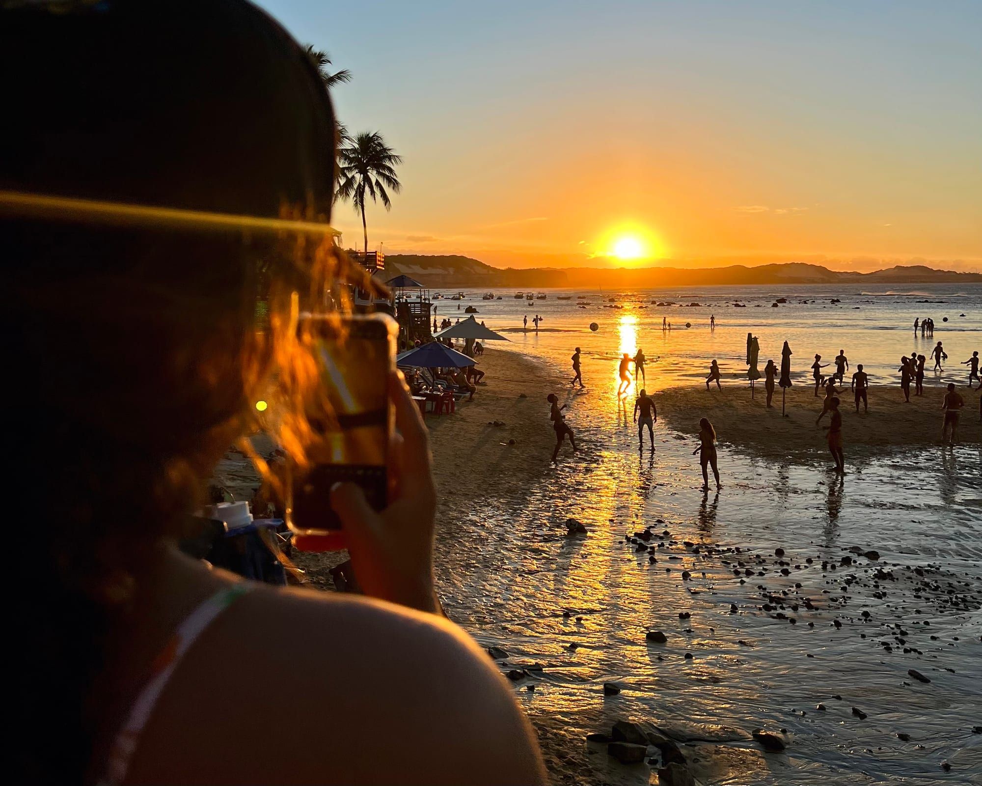 Pôr do sol na Praia do Centro da Pipa com pessoas caminhando na beira do mar