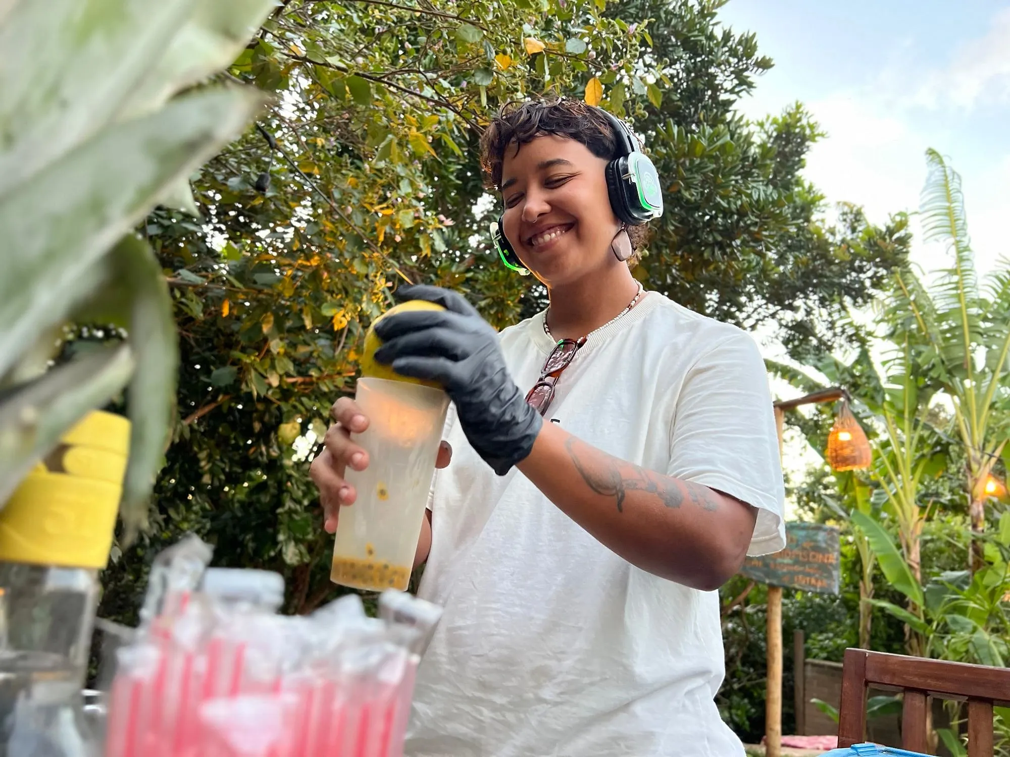 Pessoa sorrindo com fone de silent disco aceso em verde preparando um drink em edição da Silent Party, em Pipa