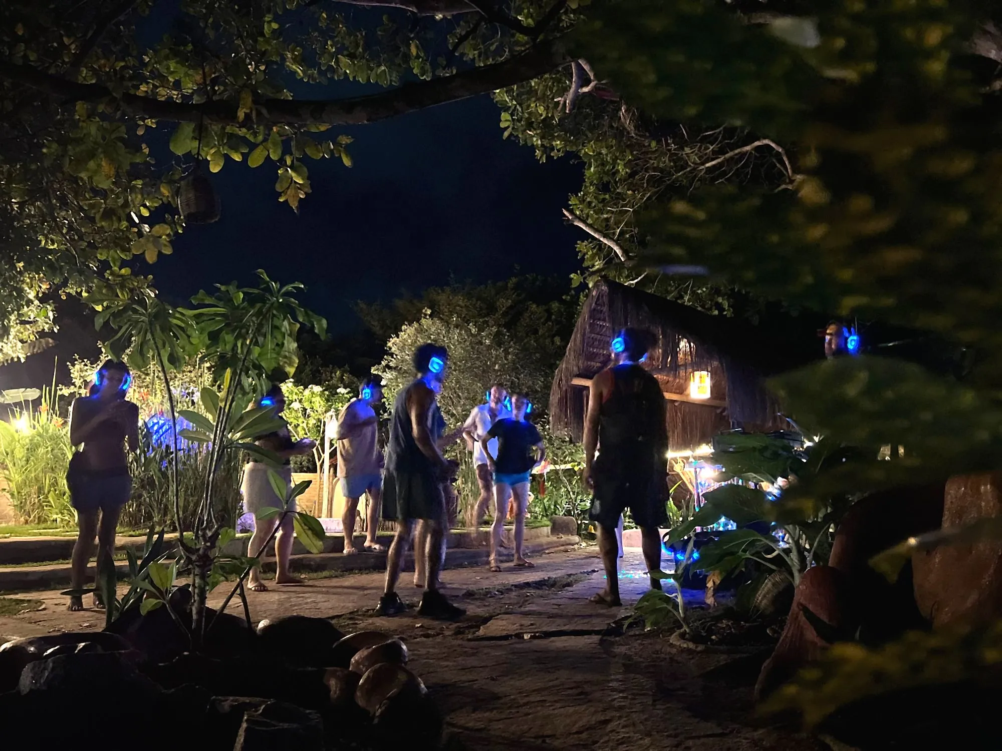 Grupo de pessoas dançando num jardim à noite, com fones de silent disco acesos em azul, em Pipa